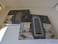 Two boxes side by side on a white surface. Each box contains three decorative floor vent covers in nickel finish with mosaic pattern.