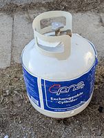 Photo of a preowned, empty propane tank with a protective metal collar and blue label reading 'Epne Exchangeable Cylinder 8 kg'