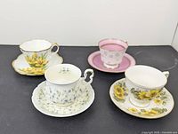 Four teacup and saucer sets with floral patterns and gold accents arranged on a black surface.