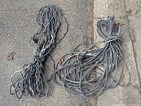 Top down photo showing two very long, heavy duty black extension cords coiled on pavement and concrete surface.