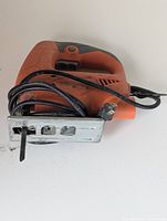 Front angle of orange and gray preowned electric jigsaw showing power cord and blade