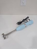 Full view of KitchenAid aqua sky hand blender lying on white surface showing blending shaft and power cord.