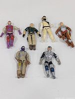 Photo showing all six vintage GI Joe miniature figurines laid on a white surface displaying varied colors and articulation points.