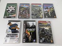 Top row with four PSP game cases: The Official Game of Poker, MX vs ATV Untamed, Capcom Classics Collection Reloaded, ATV Offroad Fury Blazin' Trails. Bottom row with three cases: Tiger Woods PGA Tour 06, Tom Clancy's Splinter Cell Essentials, SOCOM U.S. Navy SEALs Fireteam Bravo (Greatest Hits). Games appear preowned with cases intact.