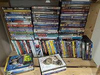 Wide shot of shelves filled with multiple stacks of DVD cases featuring movies and TV series, showing titles such as 'Contagion,' 'Crank,' 'Downton Abbey,' 'Nurse Jackie,' and others.