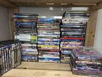 Image showing a large assortment of DVD and Blu-Ray cases on a wooden shelving unit. Various titles visible including Terminator, Dexter, Frozen, and others.