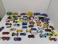 Overview of 48 assorted miniature toy cars in various colors and styles including race cars, trucks, emergency vehicles, and classic models.