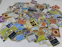 A large pile of various Pokemon cards spread on a flat surface showing many character and energy cards.