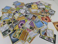 Assorted pile of Pokemon trading cards showing a variety of characters, energy, and trainer cards spread on a white surface.