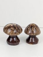 Side view of two mushroom-shaped salt and pepper shakers with brown speckled glaze and rounded caps.