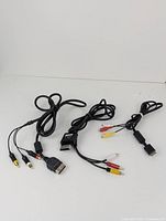 Three video game RCA adapter cables with proprietary console connectors on one end and RCA connectors on the other end, displayed coiled on a white background.
