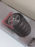 Boxed Motomaster tire rack showing 4 mounted tires for scale and mounting bracket in red and black steel tubing.