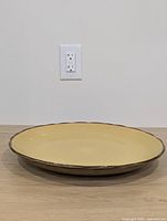 Full side view of the shallow serving bowl showing yellow color and brown rim edge against plain background.