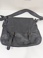 Front view of black leather satchel with two adjustable buckle straps and wide shoulder strap.