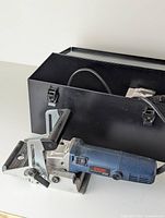 Ryobi joiner machine with attached power cord and black metal carrying case in background