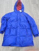 Long blue puffer coat with hood, front pockets, red interior lining, small size, new with tags visible.