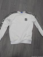 Full front view of white Adidas sweatshirt with black stripes on sleeves and logo on chest.