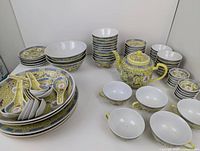 Full overview of the Asian yellow patterned dish set spread out, showing plates, bowls, spoons, cups, and teapot with detailed decoration.