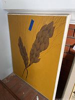 Full view of framed artwork showing two brown leaves on mustard yellow background.