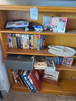 Full view of wooden bookshelf showing books, DVDs, VHS tapes, craft palette, and flashlights