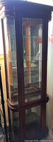 Front view of curio cabinet showing wood frame, glass door, and reflections.