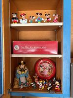Shelves with Disney character figurines on the top and bottom shelf, including Mickey, Minnie, Donald, Daisy, and Pluto. Red box present on the middle shelf for a 'First Place' award.