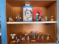 Photo showing upper and lower shelves with Disney character figurines and a ceramic cookie jar with character art and paw prints. Includes Goofy, Pluto, and others.