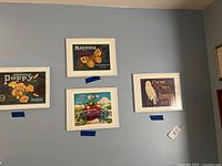 Wall-mounted framed prints of vintage fruit crate labels Poppy Brand, Mariposa Pears, Frigid Apples and Snow Owl Apples in colorful graphic style on dark backgrounds.