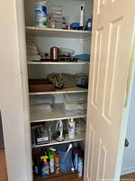 Hallway closet shelf and contents with cleaning supplies, towels, small electronics, bags, and storage containers.