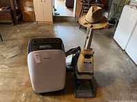 Honeywell portable AC and Hoover vacuum cleaner side by side on the floor with a cowboy hat on vacuum handle.