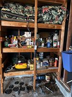 Wooden shelves filled with multiple cleaning bottles, hand sanitizer, insect sprays, and a small wooden guitar. Below, weights and hand tools are organized on lower shelves.