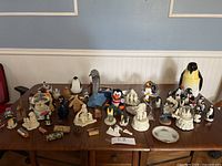 Overview of all penguin and animal figurines arranged on wooden table, shows variety and quantity