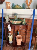 Wooden two-tier table displaying multiple pottery pieces against brick background