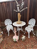 Full view of white cast iron patio set with two chairs, round table, and three decorative items placed on and around the table.
