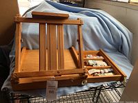 Wooden portable Aaron Brothers art easel showing adjustable wooden frame and storage compartment with paint tubes on side.
