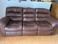 Front view of brown leather three-seat reclining sofa with visible wear on cushions and armrests