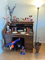 Full view of roll top desk with Disney figurines, plush bear, toys, lamp and umbrella stand, place decor on and around desk.