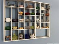 White cubed shelf filled with colorful decorative glass and ceramic items including animal-shaped vessels and various bowls and dishes