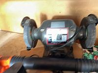 Photo of a dual wheel gray bench grinder with a worn label, placed on a wooden surface.