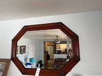 Wide shot of octagonal wall mirror hanging on white textured wall in a living room setting, showing overall shape and frame color.