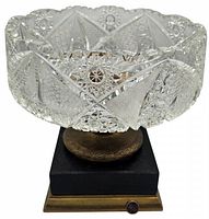 Front angle showing crystal bowl with intricate cut pattern and bronze pedestal on black stone base with brass foot plate.