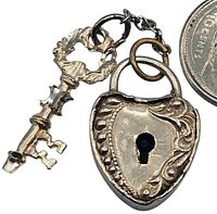 Close-up of the antique sterling miniature heart-shaped lock and matching key charm beside a coin for scale.