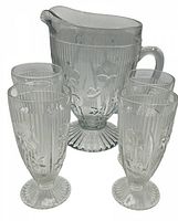 Clear glass pitcher with embossed Iris and Herringbone pattern, fluted base and handle, standing upright with five matching glasses arranged around it.