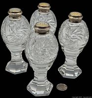 Four vintage cut glass shakers with silver tops marked Birks, showing overall condition and size compared to a coin.