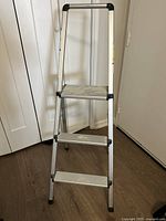 Full view of aluminum folding step ladder with three steps and black plastic corner protections.
