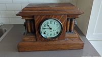 Full view of the antique Arthur Pequegnat mantel clock in oak wood with decorative columns and clock face.