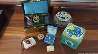 Overview of lot items including medallion in box, owl bookmark, pill boxes, potpourri dish, and tins