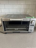 Front view of closed Breville toaster oven showing stainless steel exterior and handle, crumb debris visible inside.