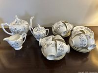 Overview of tea set items on table including teapot, sugar bowl, creamer, and multiple stacked teacups and saucers.