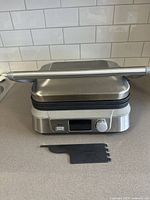 Front view of Cuisinart electric grill showing the digital display and control knob, unit is closed and plugged in.